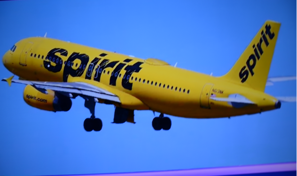 Bright yellow Spirit Airlines jet in flight against a blue sky, with large black 'Spirit' lettering on the fuselage and tail logo visible
