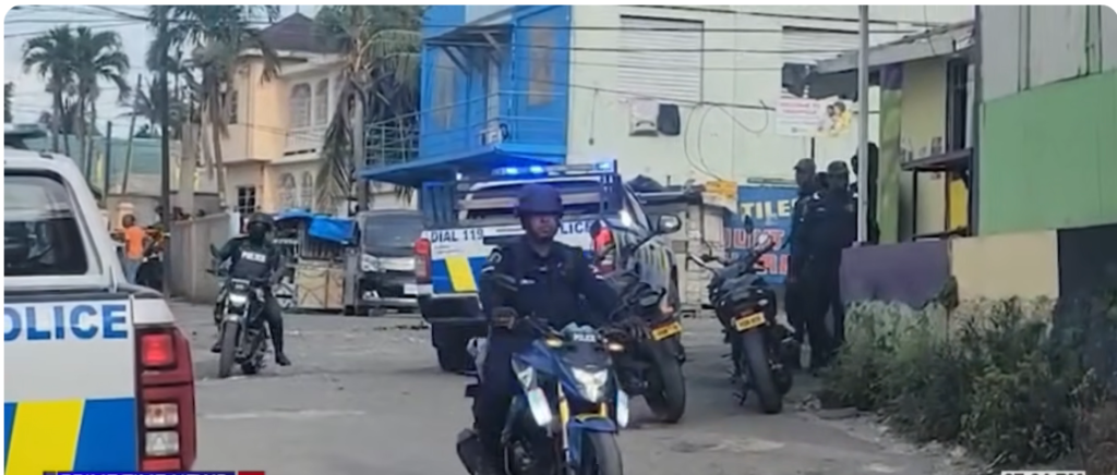 Police on motorcycles and a patrol van blocking a street; officers present in a tense urban scene.