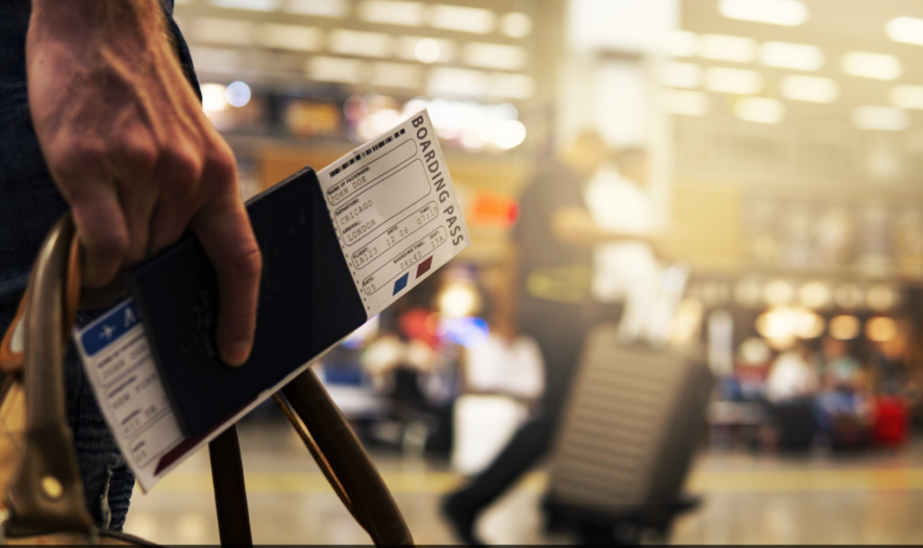 Traveler's Hand Holds a Passport and Boarding Pass at an Airport, with Blurred Passengers and Gates in the Background. Traveler's Hand Holds a Passport and Boarding Pass at an Airport, with Blurred Passengers and Gates in the Background. Traveler's Hand Holds a Passport and Boarding Pass at an Airport, with Blurred Passengers and Gates in the Background. Traveler's Hand Holds a Passport and Boarding Pass at an Airport, with Blurred Passengers and Gates in the Background.