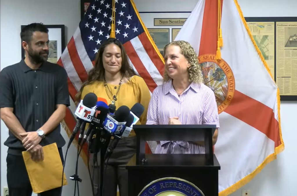 Three Speakers at a Press Conference Behind a Podium, with U.s. and Florida Flags in the Background and Multiple Microphones in Front. Three Speakers at a Press Conference Behind a Podium, with U.s. and Florida Flags in the Background and Multiple Microphones in Front.